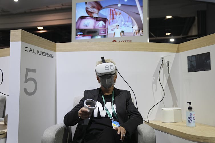 Mulher usando óculos de realidade virtual sentada em um estande de uma feira de negócios