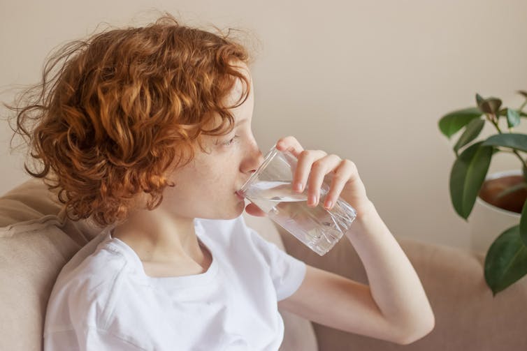 A teenage girl with flu drinks a glass of water.