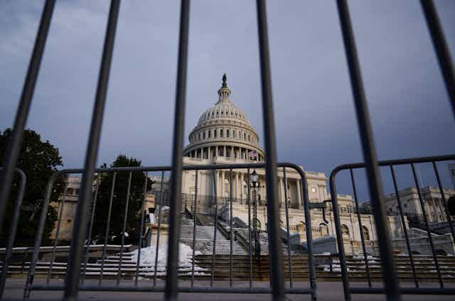 A view of the U.S. capitol building through security fencing in front of it.