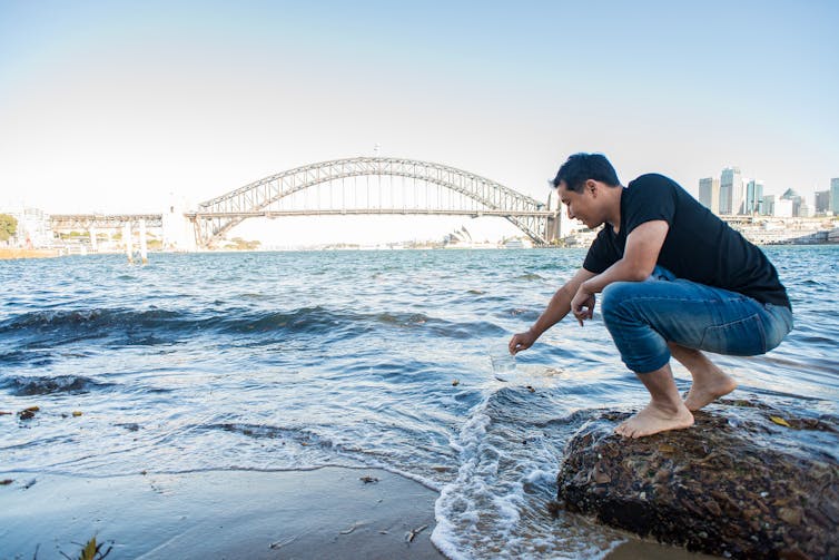 man leans towards water in front of Sydney Harbour Bridge