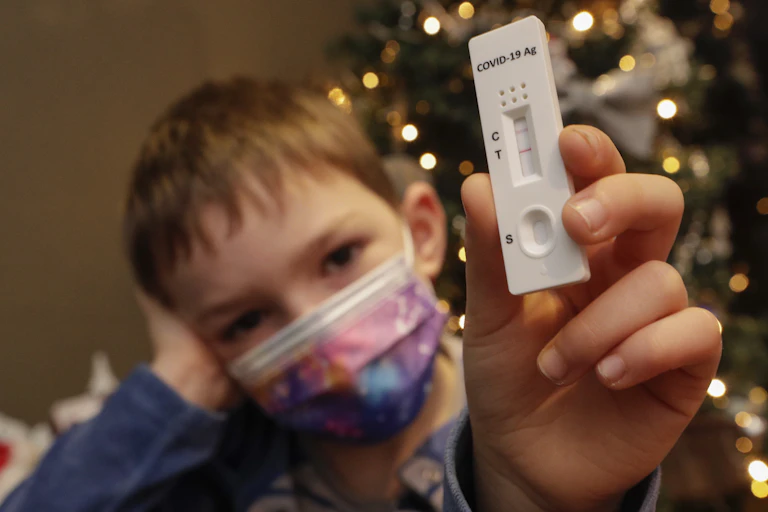 A child wearing a mask holding up a positive rapid antigen test