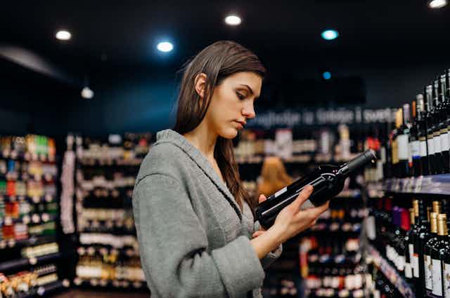 A woman reads the label on a bottle of wine in a shop.