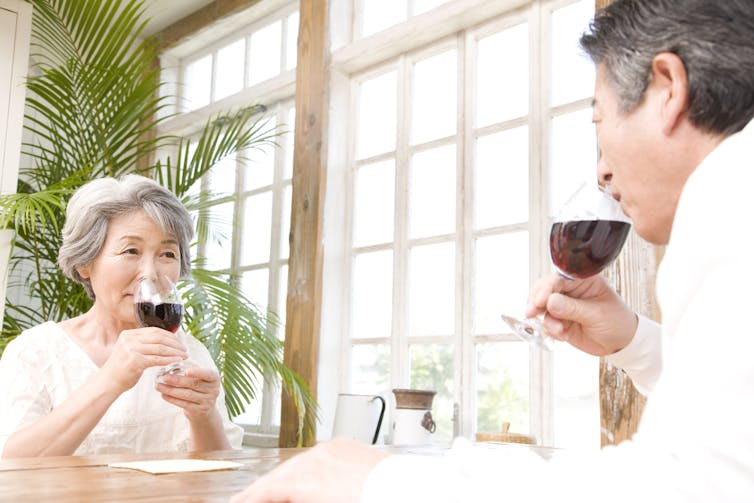 An Asian woman and Asian man drink a glass of red wine together.