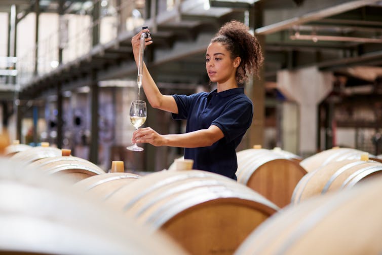 A winemaker tests wine in a factory.