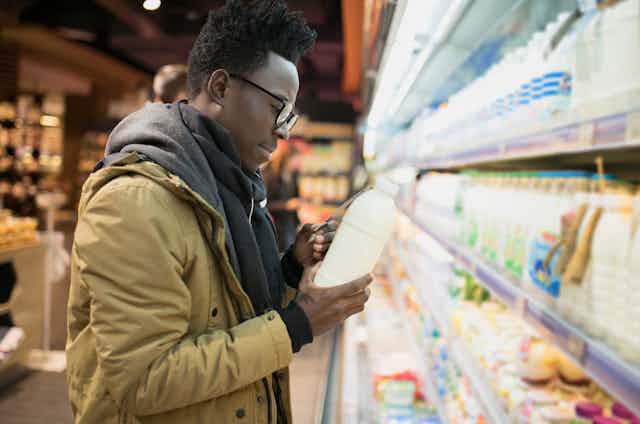 Image of a man looking at the label of a milk packet in the supermarket.