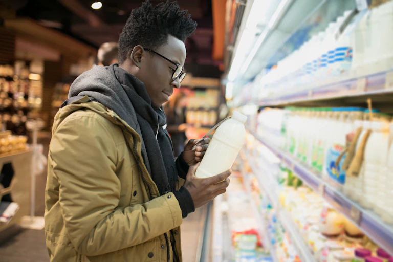 Image of a man looking at the label of a milk packet in the supermarket.