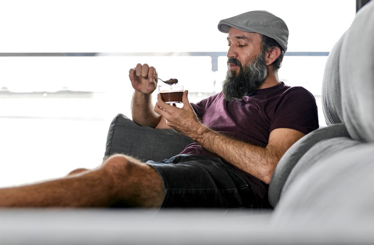 Un homme est confortablement installé sur son canapé et mange une crème au chocolat
