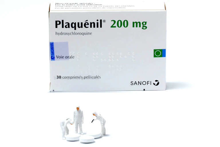 Boite de Plaquénil-Hydroxychloroquine, avec trois petits bonhommes en plastique blanc étudiant un cachet.