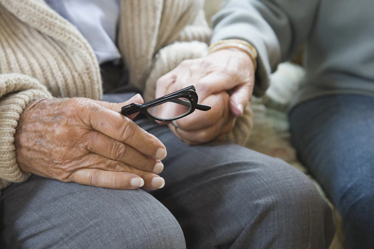 Two older people hold hands while they sit.