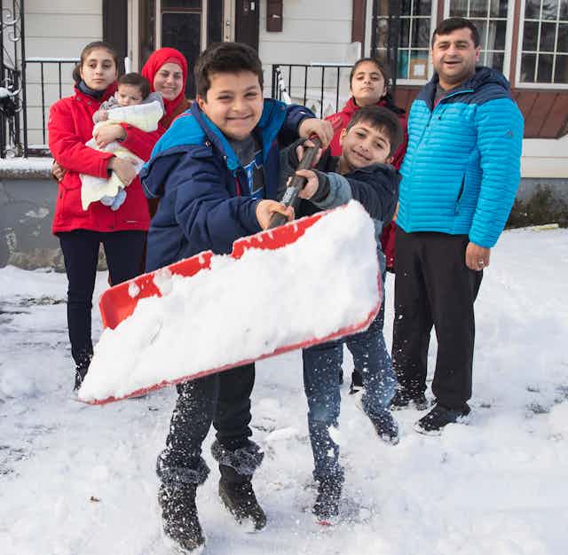 Two boys hold a shovel full of snow in front of his parents and siblings.