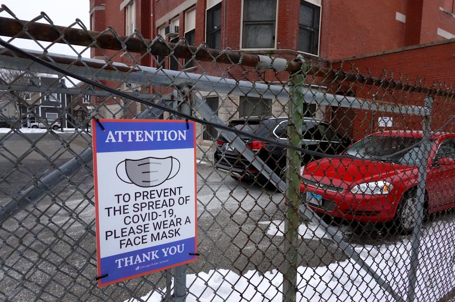 A sign on the fence outside an elementary school in Chicago asks students, staff and visitors to wear a mask to prevent the spread of COVID-19 .