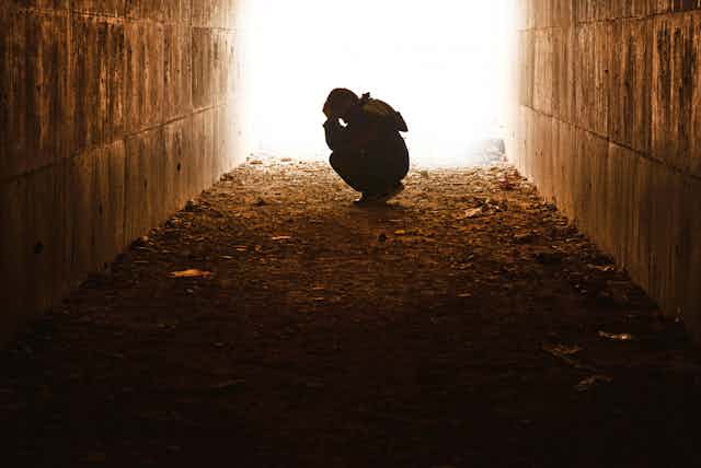 Silueta de niño solo atribulado iluminado por la boca de un túnel.