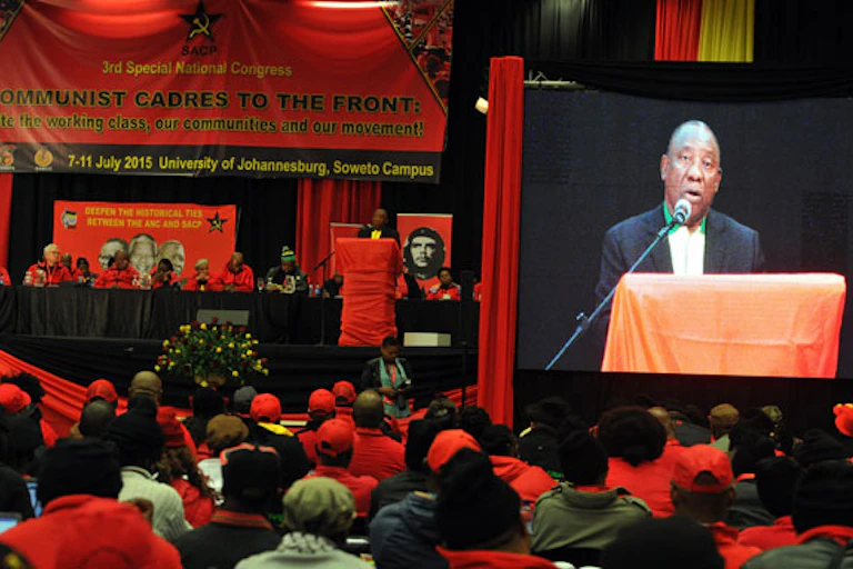 Man on stage speaking while surrounded by political party colours
