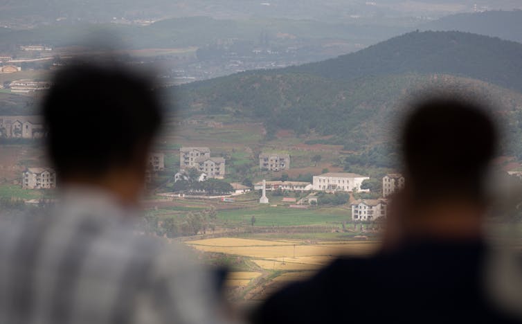 Two SOuth Koreans look from a hilltop across the demilitarised zone into North Korea.