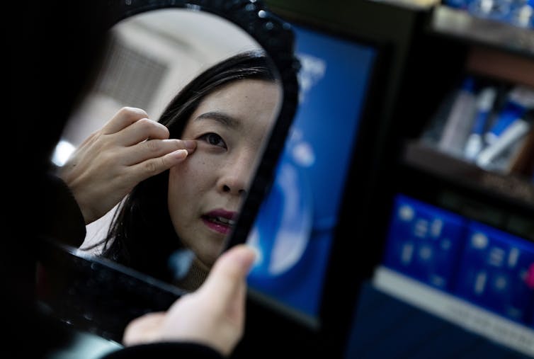 North Korean defector Kim Eun-sun touches her eye at a cosmetics shop in Seoul, South Korea