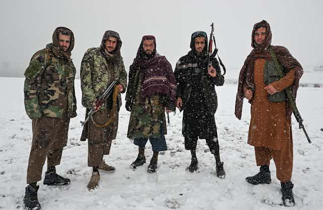 Five Taliban fighters stand in a row against a backdrop of snow, showing their guns.