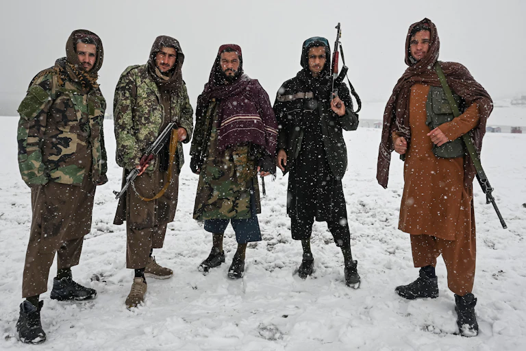 Five Taliban fighters stand in a row against a backdrop of snow, showing their guns.