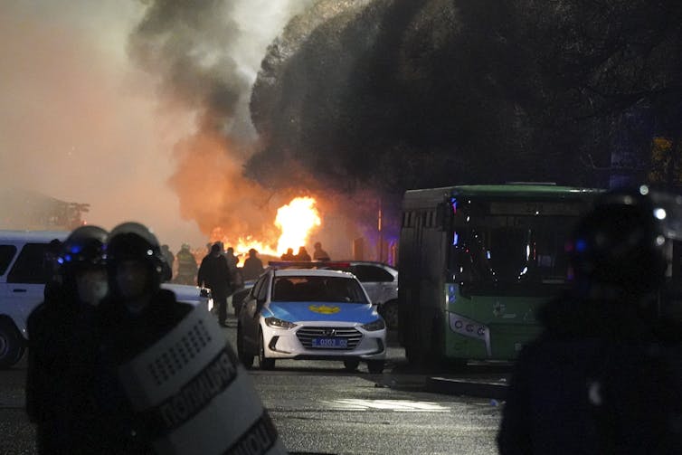 A police car on fire amid a crowd and clouds of smoke