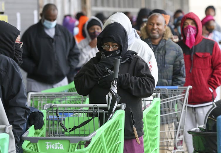 Compradores, algunos abrigados contra el frío, esperan en fila