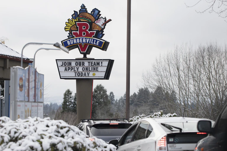 A sign seeking workers is displayed at a fast food restaurant.