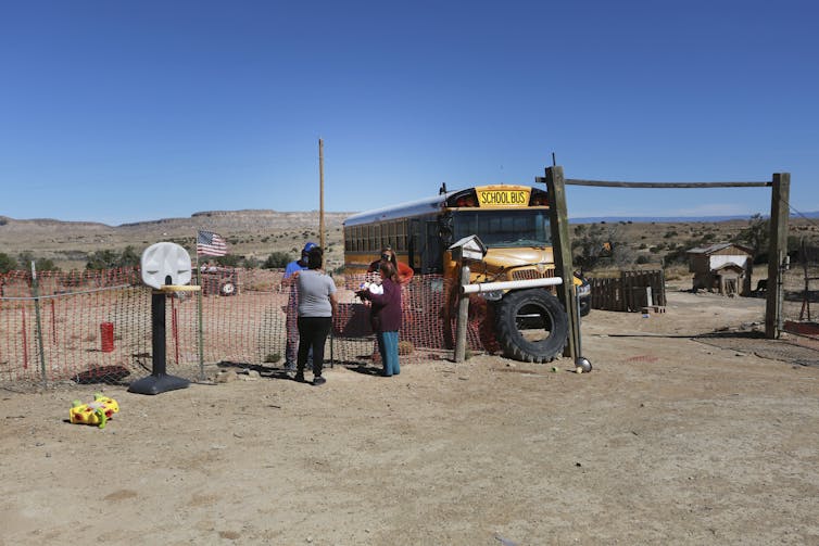 People stand outside a school bus in a rural area