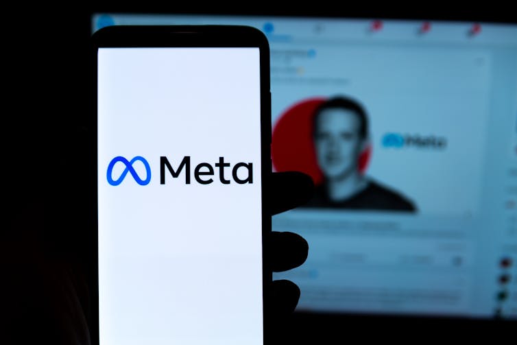 Teléfono con el logo de Meta y al fondo, difuminada, la foto de Marc Zuckerberg en Facebook.