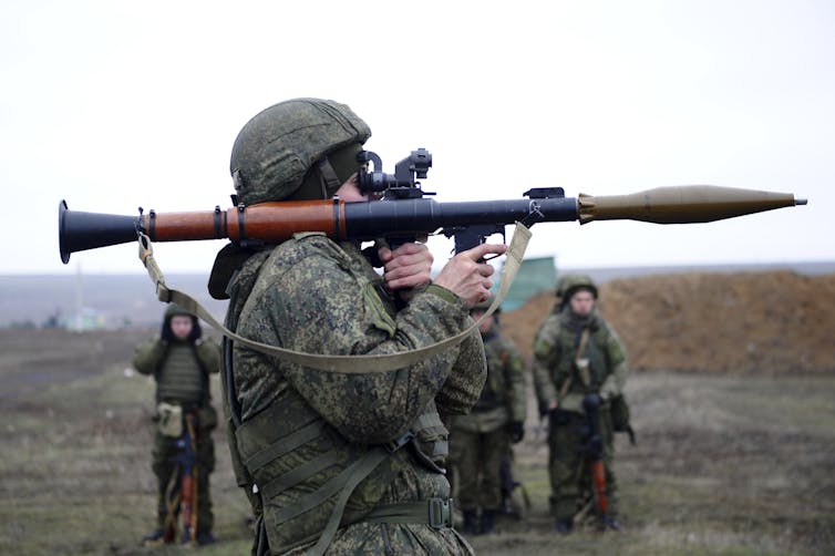 Several Russian troops in camouflage uniforms standing in a field with one holding a shoulder-held weapon.