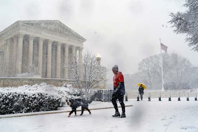 A man walks his dog past the Supreme Court as a winter storm delivers heavy snow to Capitol Hill in Washington.