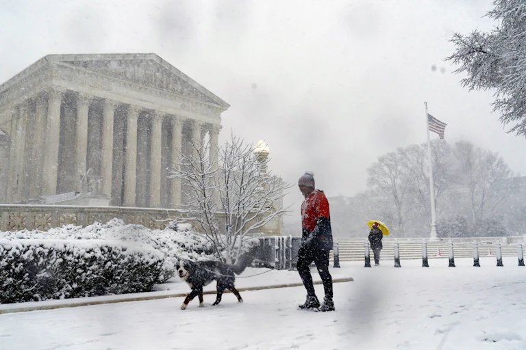 A man walks his dog past the Supreme Court as a winter storm delivers heavy snow to Capitol Hill in Washington.