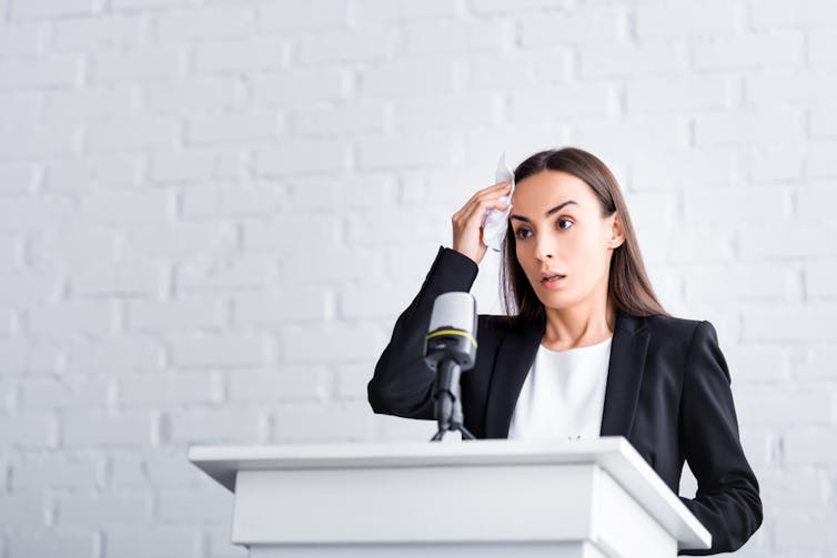 Woman giving a public speech, wiping her forehead