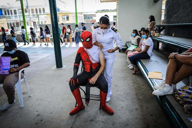 A man in a spiderman outfit gets vaccinated