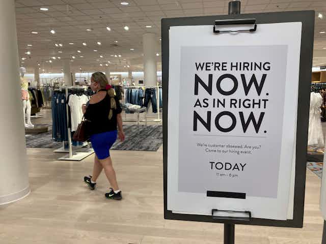 A female customer walks behind a sign at a Nordstrom store that says “We’re hiring now. As in right now’ in Coral Gables, Florida