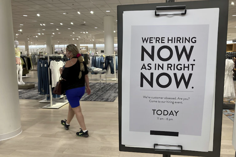 A female customer walks behind a sign at a Nordstrom store that says “We’re hiring now. As in right now’ in Coral Gables, Florida