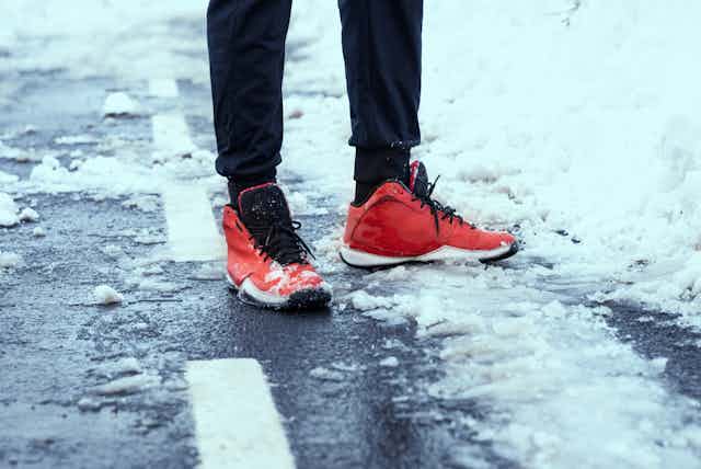 A person in red running shoes stands on a snowy road