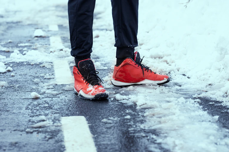 A person in red running shoes stands on a snowy road