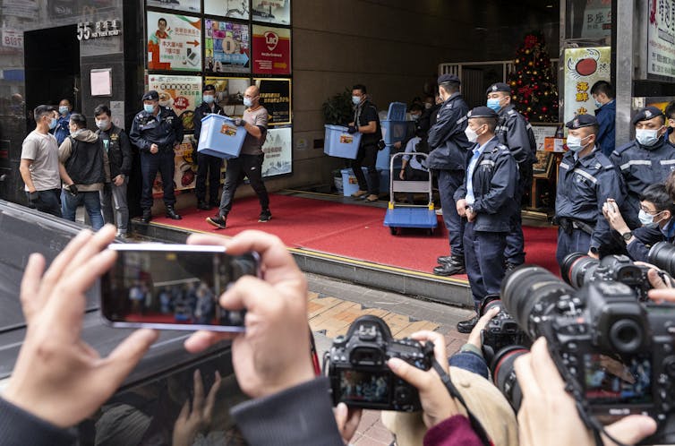 Police leaving the Stand News offices carrying large boxes of documents while a crowd looks on