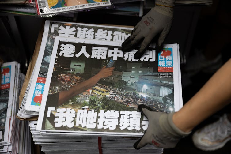 A close-up on the hands of a worker arranging a stack of Apple Daily newspapers