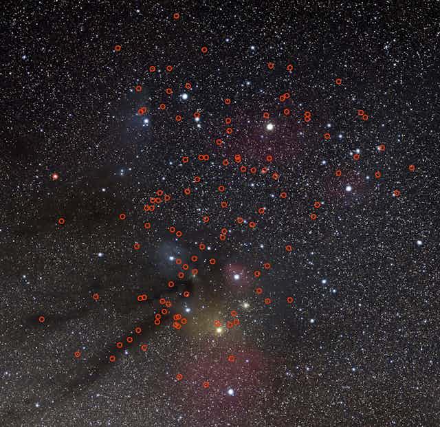 Telescope image of a cluster of stars, with red circles overlaid indicating the location of possible planets. 
