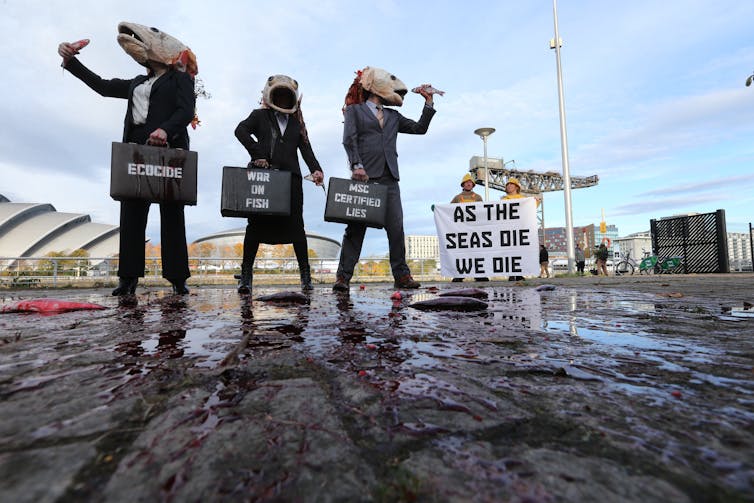 protestors outside COP26 wearing papier mâché fish heads.