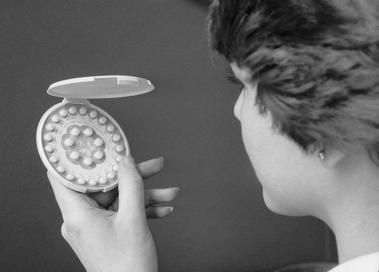 A black and white photo shows a woman facing an open birth control package