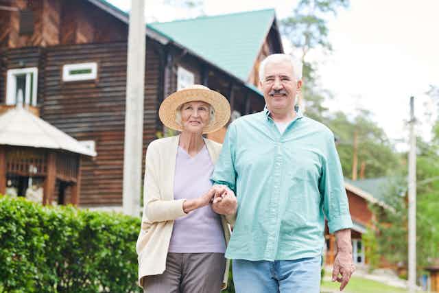 A senior couple walks arm in arm in front of a compound.