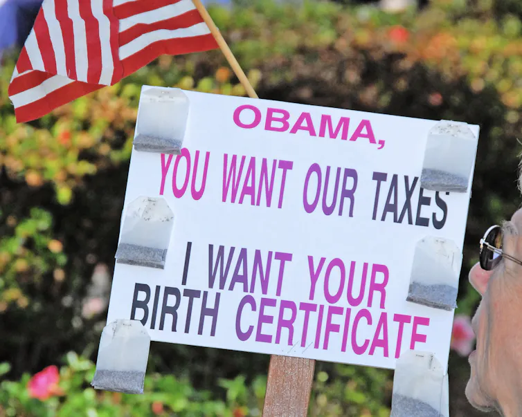 A sign reads 'Obama, you want our taxes. I want your birth certificate.'