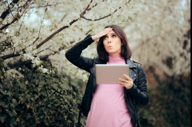 A woman looks at a tablet and holds her hand to her head