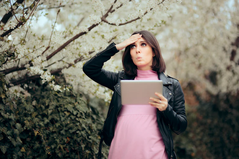A woman looks at a tablet and holds her hand to her head