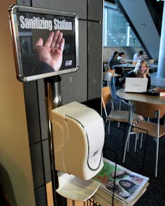 Students sit near a hand sanitizer dispenser at a university.