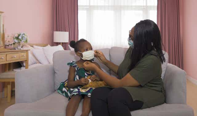 A woman and child sit at home wearing surgical masks.
