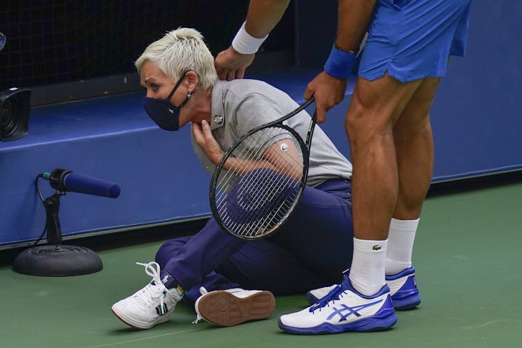 Novak Djokovic verifica um juiz de linha depois de atingi-la com uma bola.