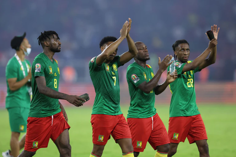 Four footballers in uniform look tired and pleased as they walk together across the field, some clapping, their hands in the air.