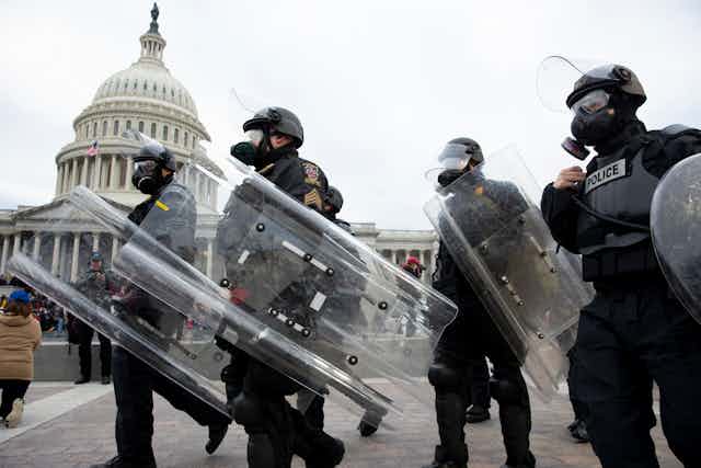 US police in gas masks and riot shields on January 6, 2021 with the US capitol building in the background