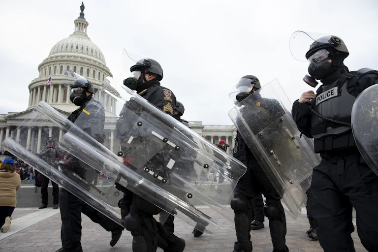 US police in gas masks and riot shields on January 6, 2021 with the US capitol building in the background